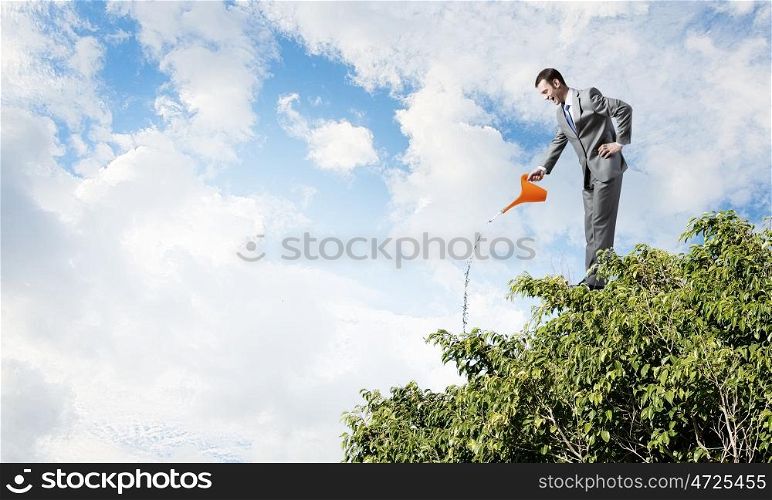 Make your income grow. Young cheerful businessman watering green tree with can
