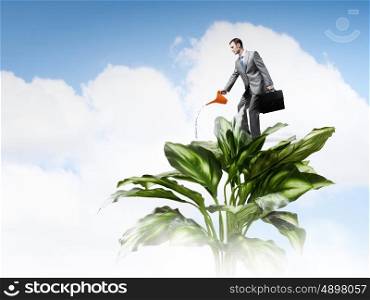 Make your income grow. Young cheerful businessman watering green tree with can
