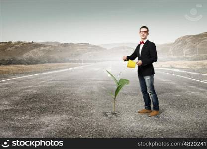Make your income grow. Young man pouring water on growing from asphalt tree