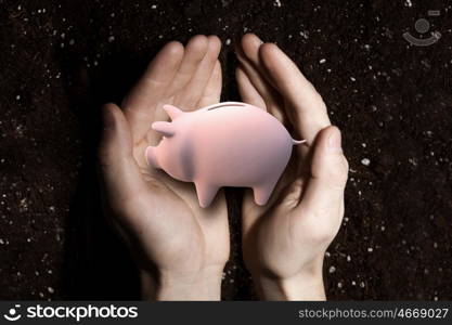 Make your savings grow. Close up of malepalms holding piggy bank and soil at background