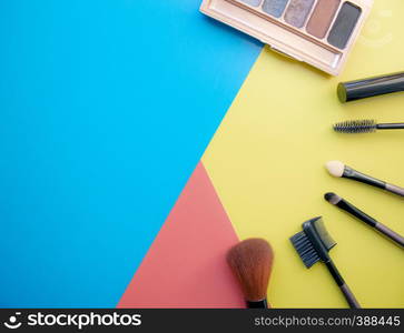 Makeup and makeup brushes, eye shadows on a colored background. Cosmetics for the face. With empty space on the left. View from above. Makeup and makeup brushes, eye shadows on a colored background. Cosmetics for the face. With empty space on the left.