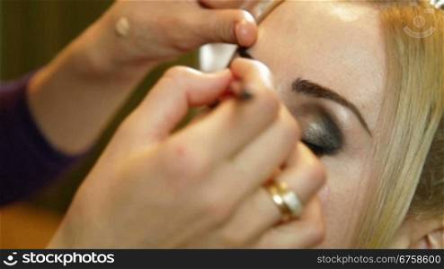 Makeup artist applied eyeshadow to an attractive young bride eyelids