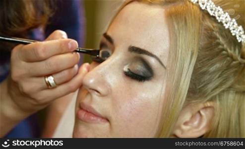 Makeup artist applied eyeshadow to an attractive young bride eyelids