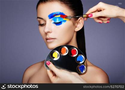 Makeup artist applies colorful makeup. Fashion model woman with colored face painted. Beauty art portrait of beautiful model with colorful abstract makeup