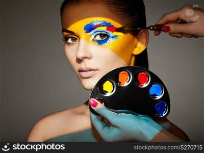 Makeup artist applies colorful makeup. Fashion model woman with colored face painted. Beauty art portrait of beautiful model with colorful abstract makeup