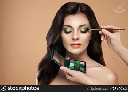 Makeup artist applies eye shadow. Beautiful woman face. Perfect makeup. Make-up detail. Beauty girl with perfect skin. Nails and manicure. Eye shadow palette