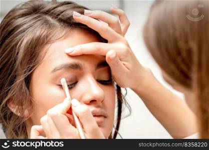 Makeup artist applies eye shadow with a brush on the eye of a beautiful young caucasian woman against a white background. Makeup artist applies eye shadow