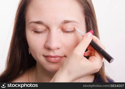 Makeup artist applies foundation of a beautiful young girl in the makeup