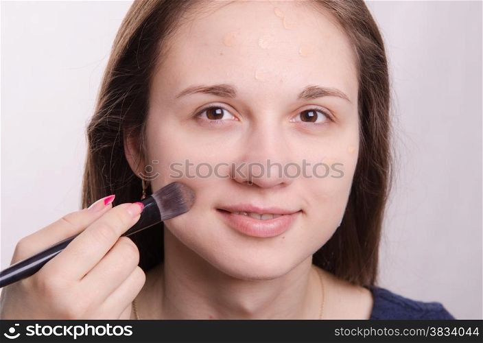 Makeup artist applies foundation of a beautiful young girl in the makeup