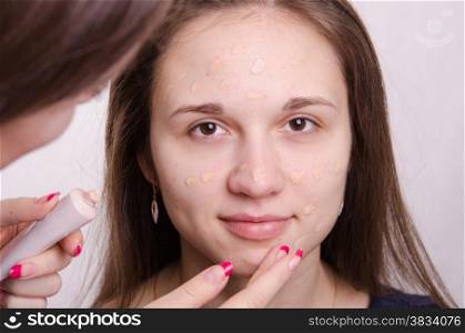 Makeup artist applies foundation of a beautiful young girl in the makeup