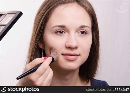Makeup artist applies powder on the face of a beautiful young girl in the makeup