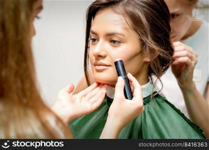 Makeup artist applying cream blush stick foundation on cheek of young caucasian woman. Makeup artist applying cream blush stick