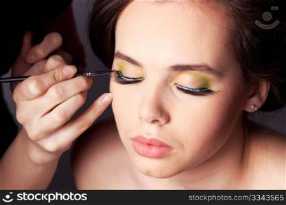 Makeup artist applying eye shadow to a young female model.