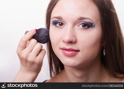 Makeup artist brush powder gets on the face of a beautiful young girl in the makeup