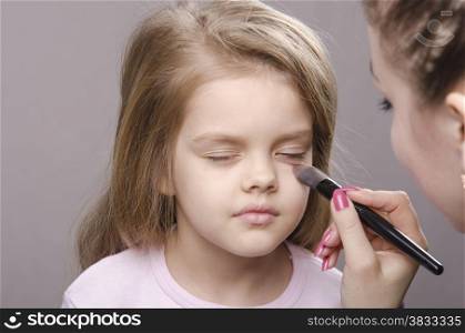 Makeup artist deals powder brush on the face of a five year old girl