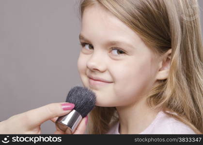 Makeup artist deals powder brush on the face of a five year old girl