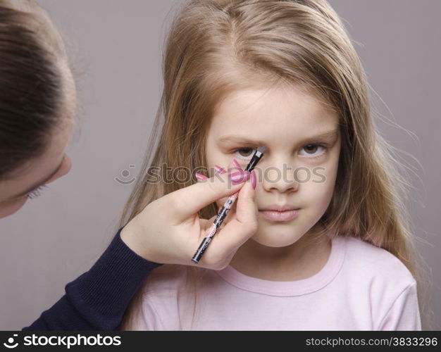 Makeup artist in the process of makeup brings eyebrows on the face five year old girl