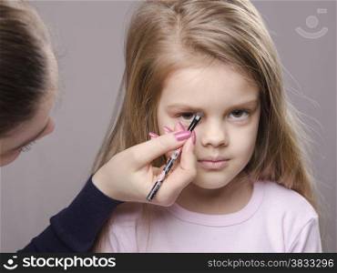 Makeup artist in the process of makeup brings eyebrows on the face five year old girl