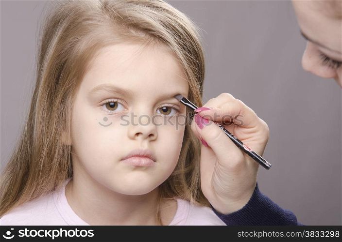 Makeup artist in the process of makeup brings eyebrows on the face five year old girl