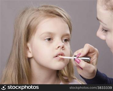 Makeup artist in the process of makeup causes Shine on the lips five year old girl