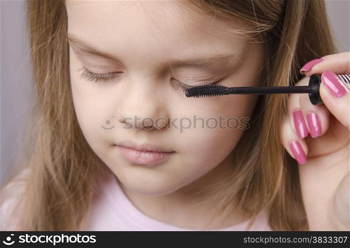 Makeup artist in the process of makeup colors eyelashes on the face five year old girl