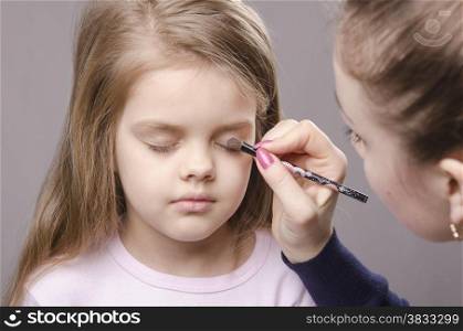 Makeup artist in the process of makeup colors eyelids on the face five year old girl