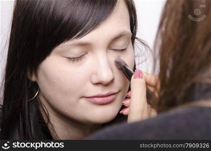 Makeup artist in the process of makeup, does the powder on the face of a beautiful girl. The girl looks frame