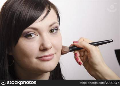 Makeup artist in the process of makeup, does the powder on the face of a beautiful girl. The girl looks frame