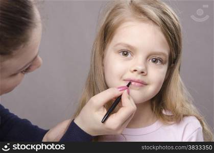 Makeup artist in the process of makeup lipstick five year old girl
