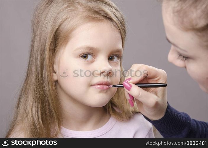 Makeup artist in the process of makeup lipstick five year old girl