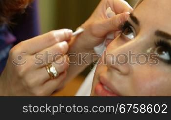 makeup artist is using a brush to apply makeup to an attractive young woman&acute;s eyelids