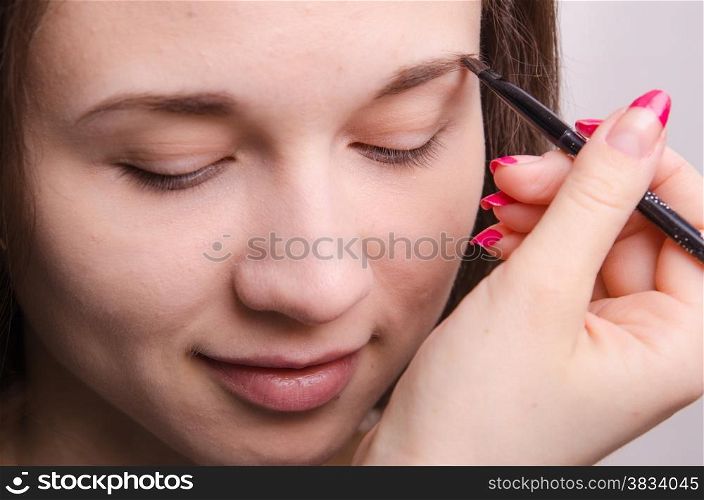 Makeup artist paints the eyebrows of a beautiful young girl in the makeup