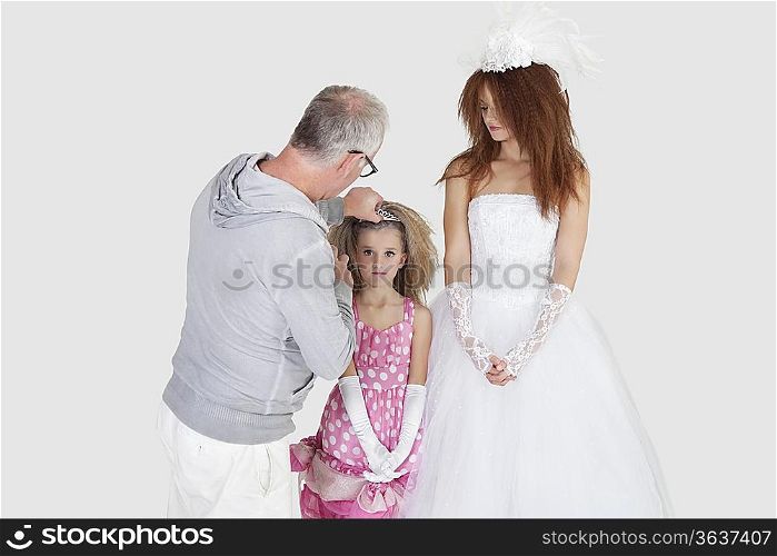Makeup artist with spraying on bridesmaid&acute;s hair while bride looking over gray background