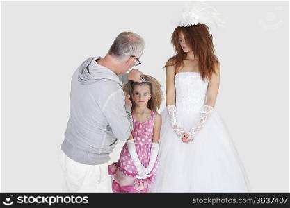 Makeup artist with spraying on bridesmaid&acute;s hair while bride looking over gray background