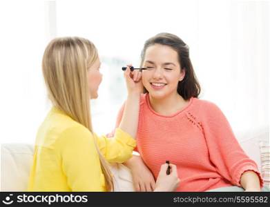 makeup, friendship and leisure concept - two smiling teenage girls applying make up at home