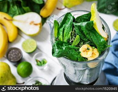 Making a healthy detox drink in a blender - smoothie with fresh fruits, green spinach and superfood seeds. Healthy lifestyle concept, ingredients for smoothies on the table, top view