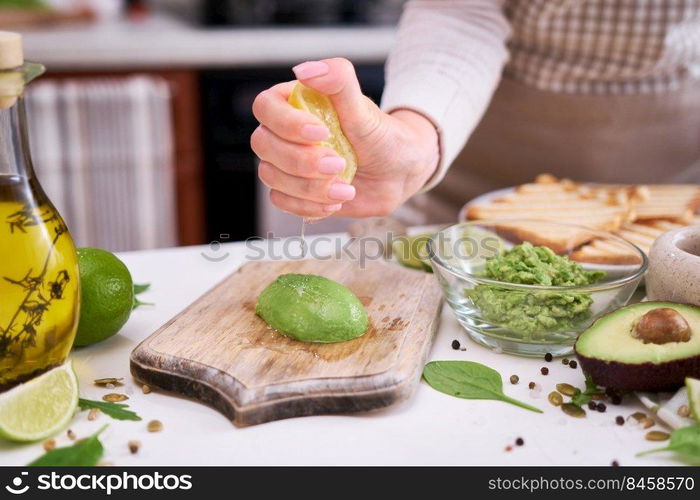 Making avocado toast - Woman squeezing fresh lime juice onto ripe halved avocado.. Making avocado toast - Woman squeezing fresh lime juice onto ripe halved avocado