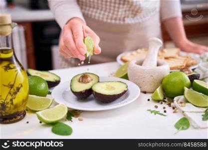 Making avocado toast - Woman squeezing fresh lime juice onto ripe halved avocado.. Making avocado toast - Woman squeezing fresh lime juice onto ripe halved avocado