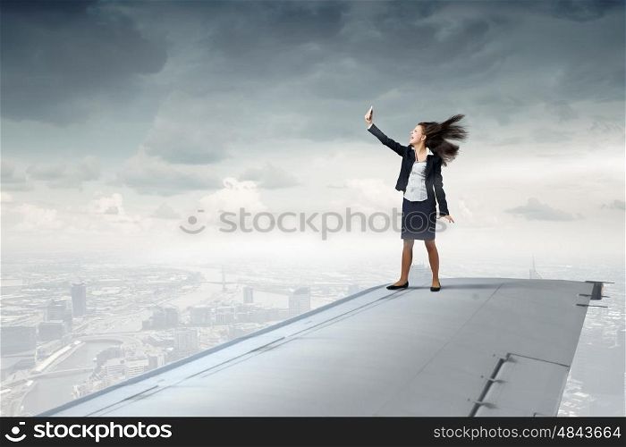 Making best selfie photo. Businesswoman standing on airplane wing and taking selfie