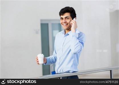 Making calls. Young man with coffee in hand talking on mobile phone