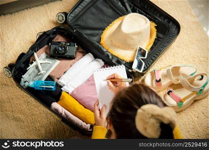 Making check list of things to pack for travel. Woman writing paper take note and packing suitcase to vacation writing paper list sitting on room, prepare clothes into luggage, Travel vacation travel