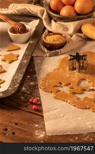 Making christmas gingerbread cookies. Raw dough in shape of gingerbread man, christmas tree, star, snowflakes on paper on tray on rustic table with rolling pin. Preparing for baking