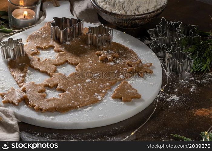 Making christmas gingerbread cookies. Raw dough in shape of gingerbread man, christmas tree, star, snowflakes on paper on tray on rustic table with rolling pin. Preparing for baking