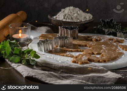 Making christmas gingerbread cookies. Raw dough in shape of gingerbread man, christmas tree, star, snowflakes on paper on tray on rustic table with rolling pin. Preparing for baking