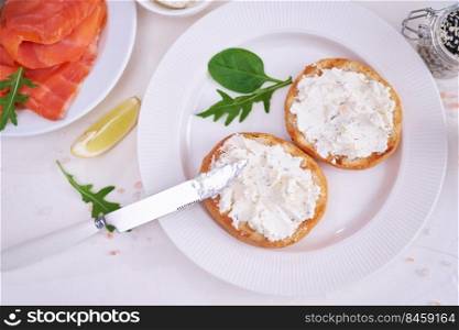 Making cream cheese and salmon toatst - woman smearing cream cheese on a grilled bun.. Making cream cheese and salmon toatst - woman smearing cream cheese on a grilled bun