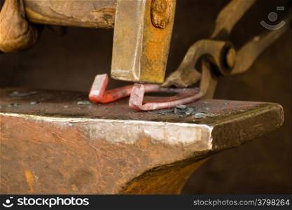 Making decorative element in the smithy on the anvil. Hammering glowing steel. Blacksmith forges a hot horseshoe.