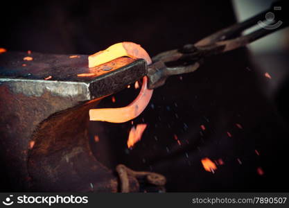 Making decorative element in the smithy on the anvil. Hammering glowing steel. Blacksmith forges a hot horseshoe.