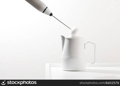 Making foamy milk with milk frother on a white table.