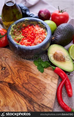making guacamole - crushed avocado in marble mortar and ingredients.. making guacamole - crushed avocado in marble mortar and ingredients