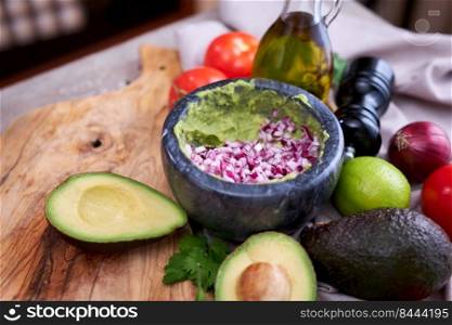 making guacamole - crushed avocado in marble mortar and ingredients.. making guacamole - crushed avocado in marble mortar and ingredients